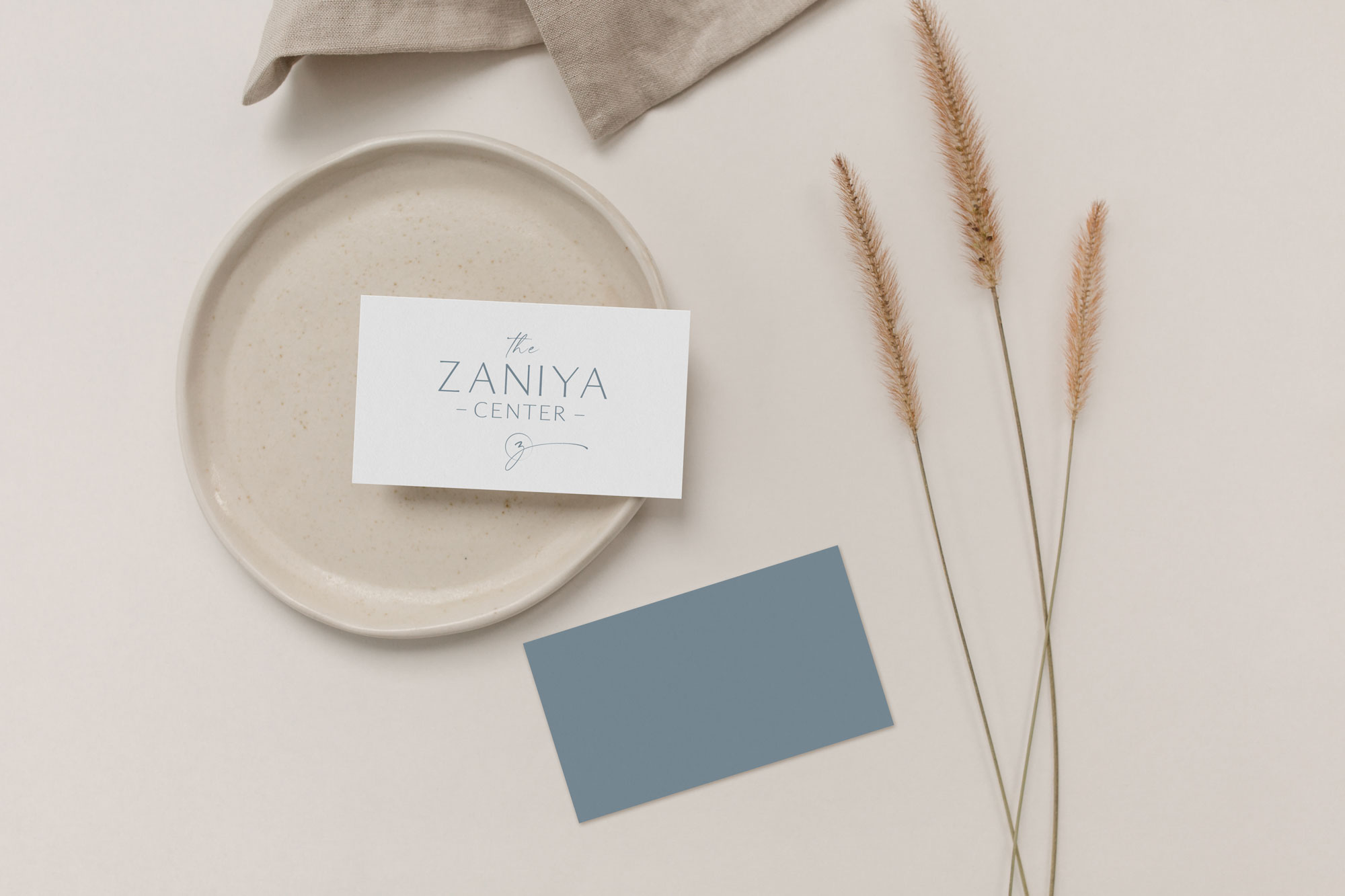 Business card featuring the Zaniya Center logo sitting on a handmade ceramic place on a tan background.
