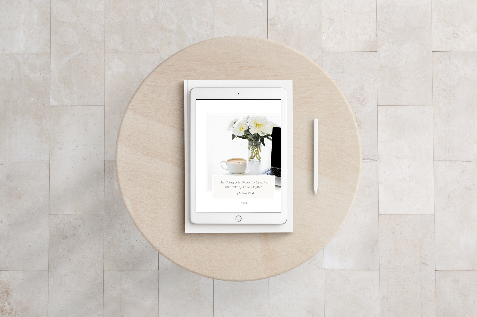 Ipad on round wooden table with image of a cup of coffee, bouquet of flowers and laptop