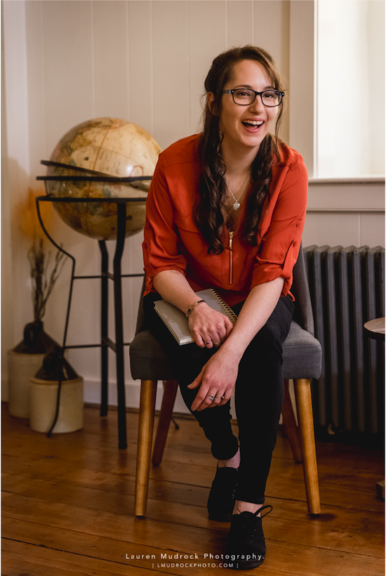 Woman sitting on a chair leaning forward and laughing with a globe of the earth on a stand in the background.
