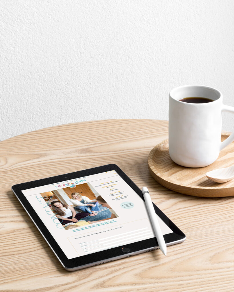 ipad displaying Colorful Minds website on wooden table next to a mug of coffee.