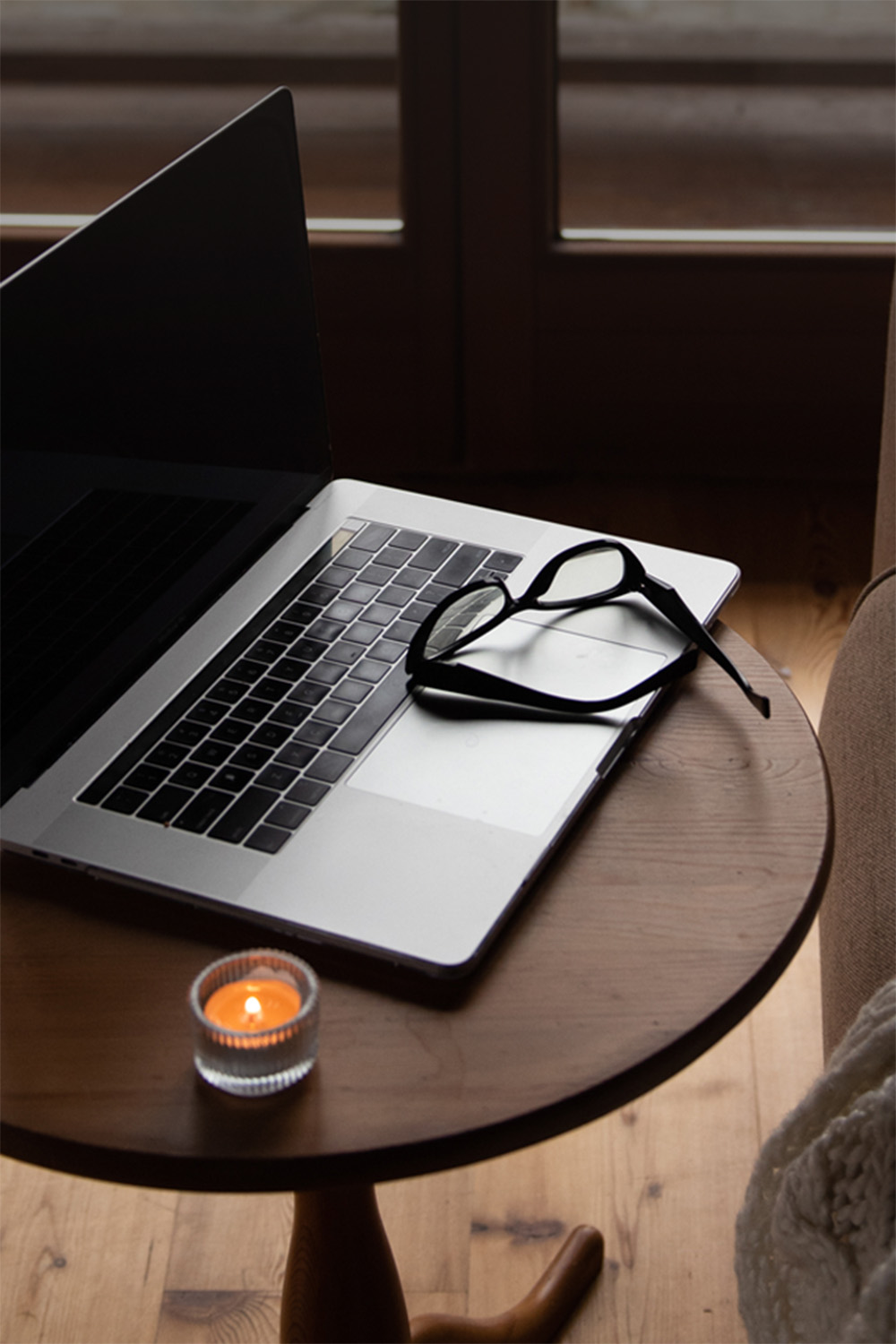 Macbook sitting on a wooden table next to a burning candle.